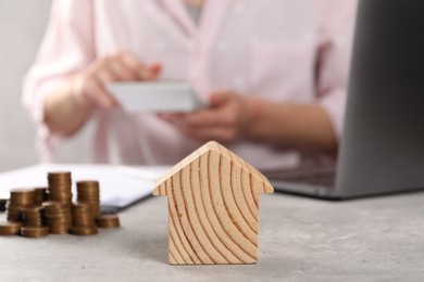 Woman calculating money at grey table, focus on wooden house model