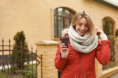 Young woman with cup of coffee walking outdoors. Space for text