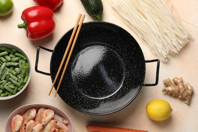 Black wok, chopsticks and products on color table, flat lay