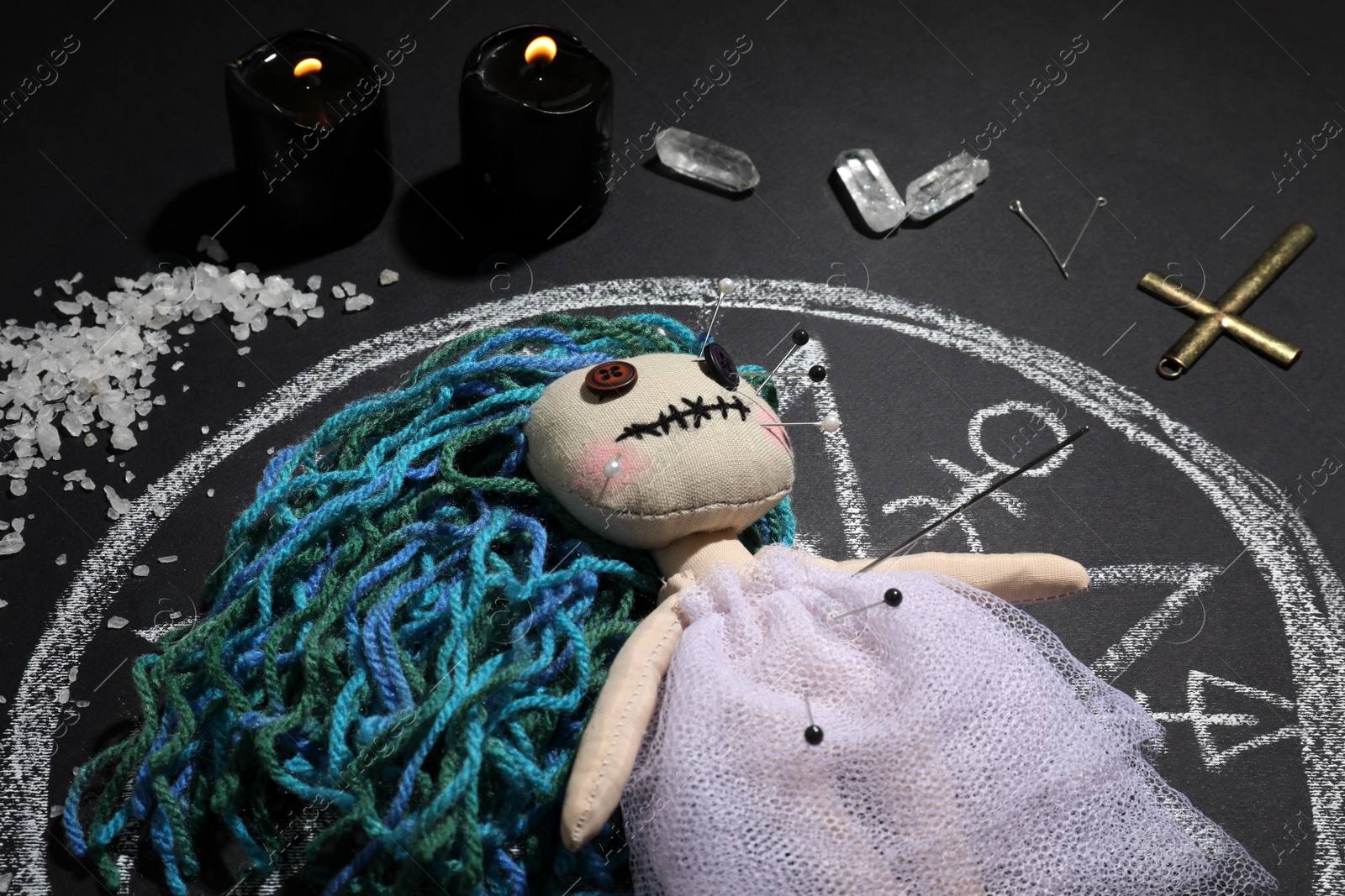 Photo of Female voodoo doll with pins surrounded by ceremonial items on black background