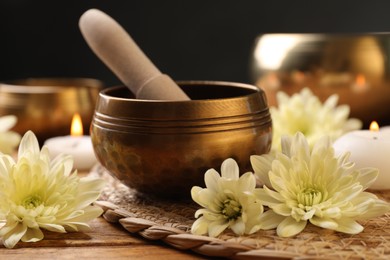 Tibetan singing bowl with mallet and beautiful chrysanthemum flowers on wooden table, closeup