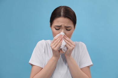 Photo of Woman blowing nose on light blue background. Cold symptoms