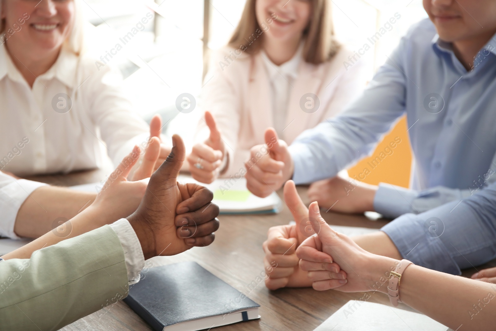 Photo of People showing thumbs up at table, closeup of hands. Unity concept