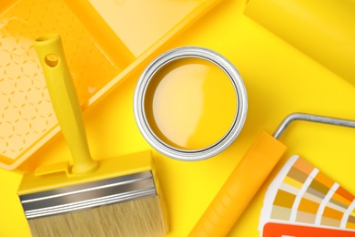 Flat lay composition with can of paint, brush and renovation tools on yellow background