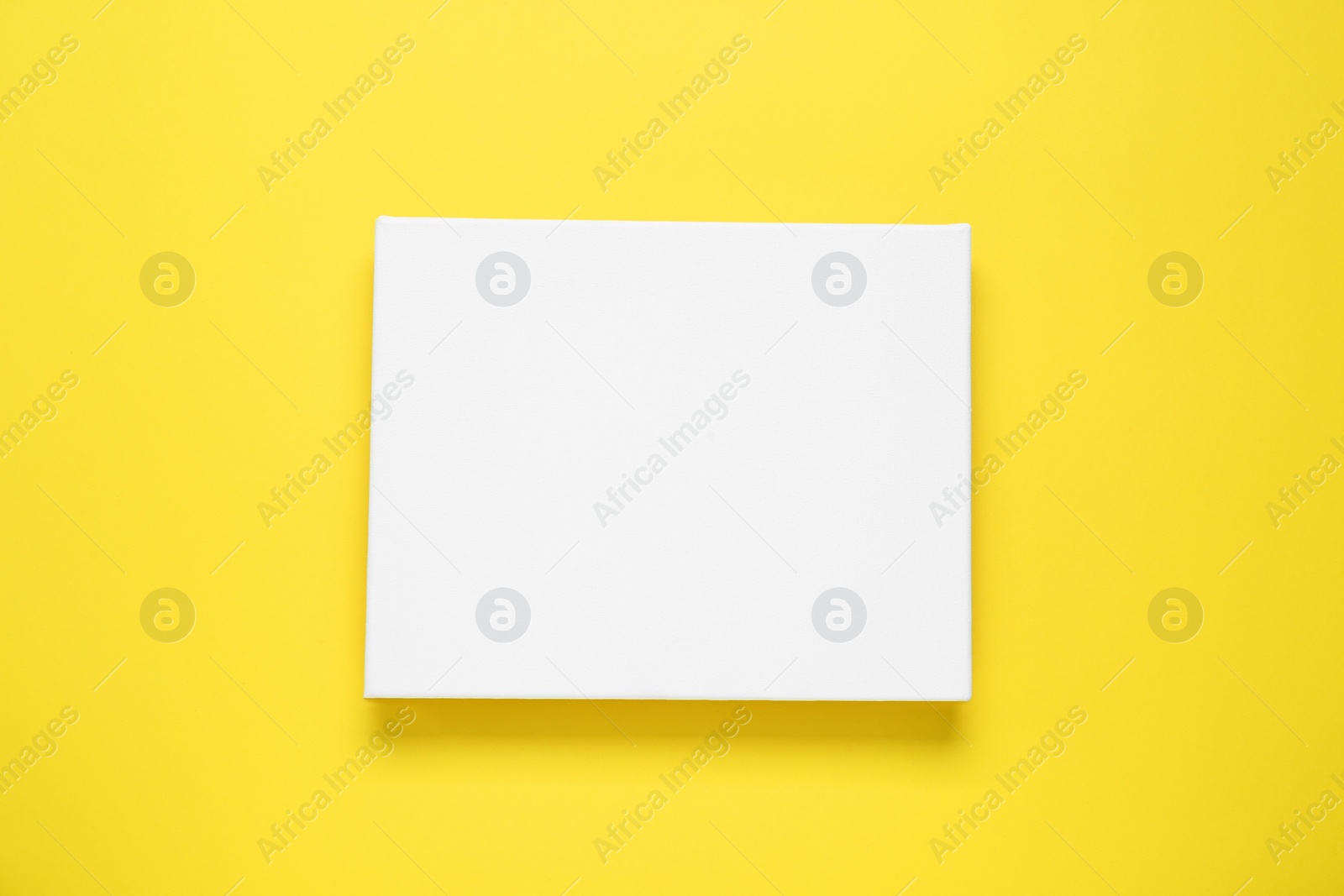 Photo of Blank canvas on yellow background, top view. Space for design