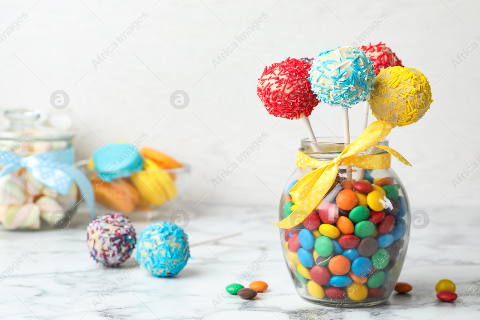 Photo of Yummy bright cake pops in glass jar full of candies on table. Space for text