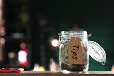 Photo of Glass jar with tips on wooden table indoors. Space for text