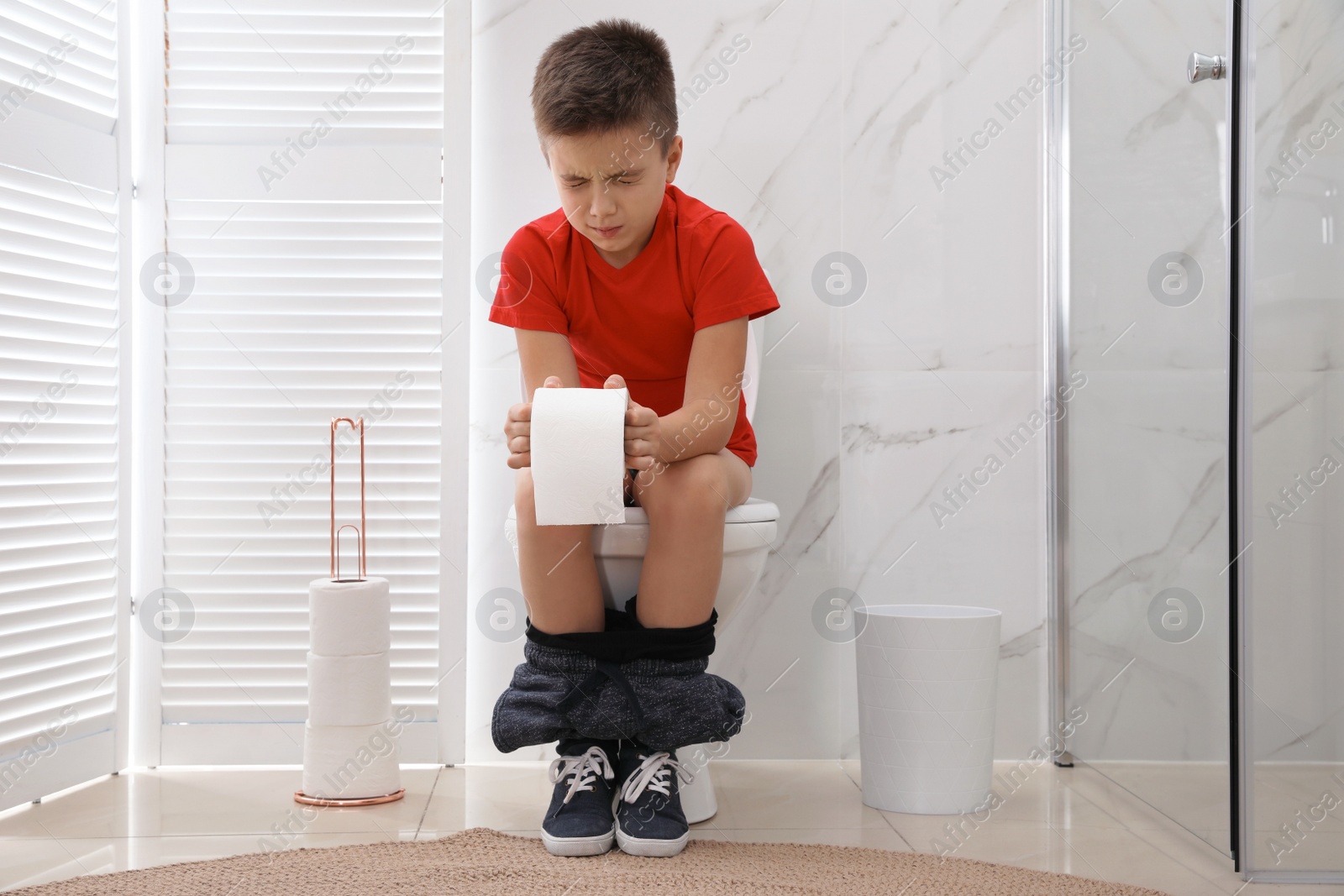 Photo of Boy with paper suffering from hemorrhoid on toilet bowl in rest room