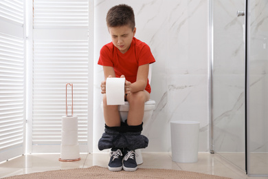 Photo of Boy with paper suffering from hemorrhoid on toilet bowl in rest room