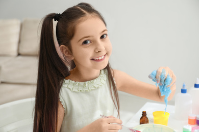 Photo of Cute little girl making DIY slime toy at table in room