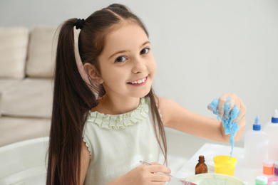 Cute little girl making DIY slime toy at table in room