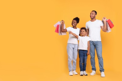 Photo of Family shopping. Happy parents and son with colorful bags on orange background, space for text