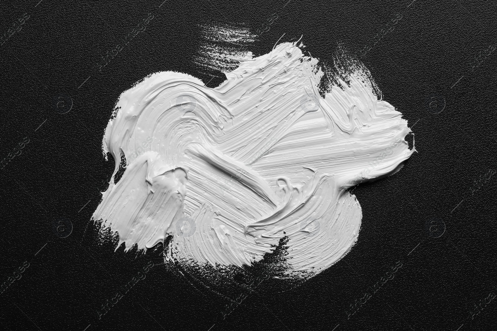 Photo of Strokes of white oil paint on black canvas, top view