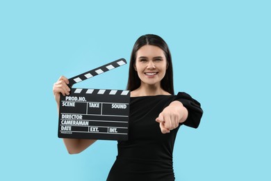 Happy actress with clapperboard on light blue background. Film industry