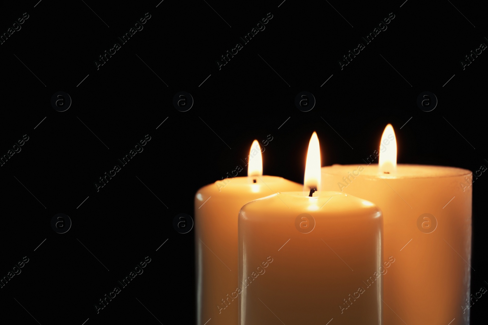 Photo of Wax candles burning on black background, closeup