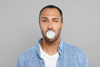 Portrait of young man blowing bubble gum on light grey background