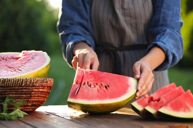 Woman cutting tasty ripe watermelon at wooden table outdoors, closeup