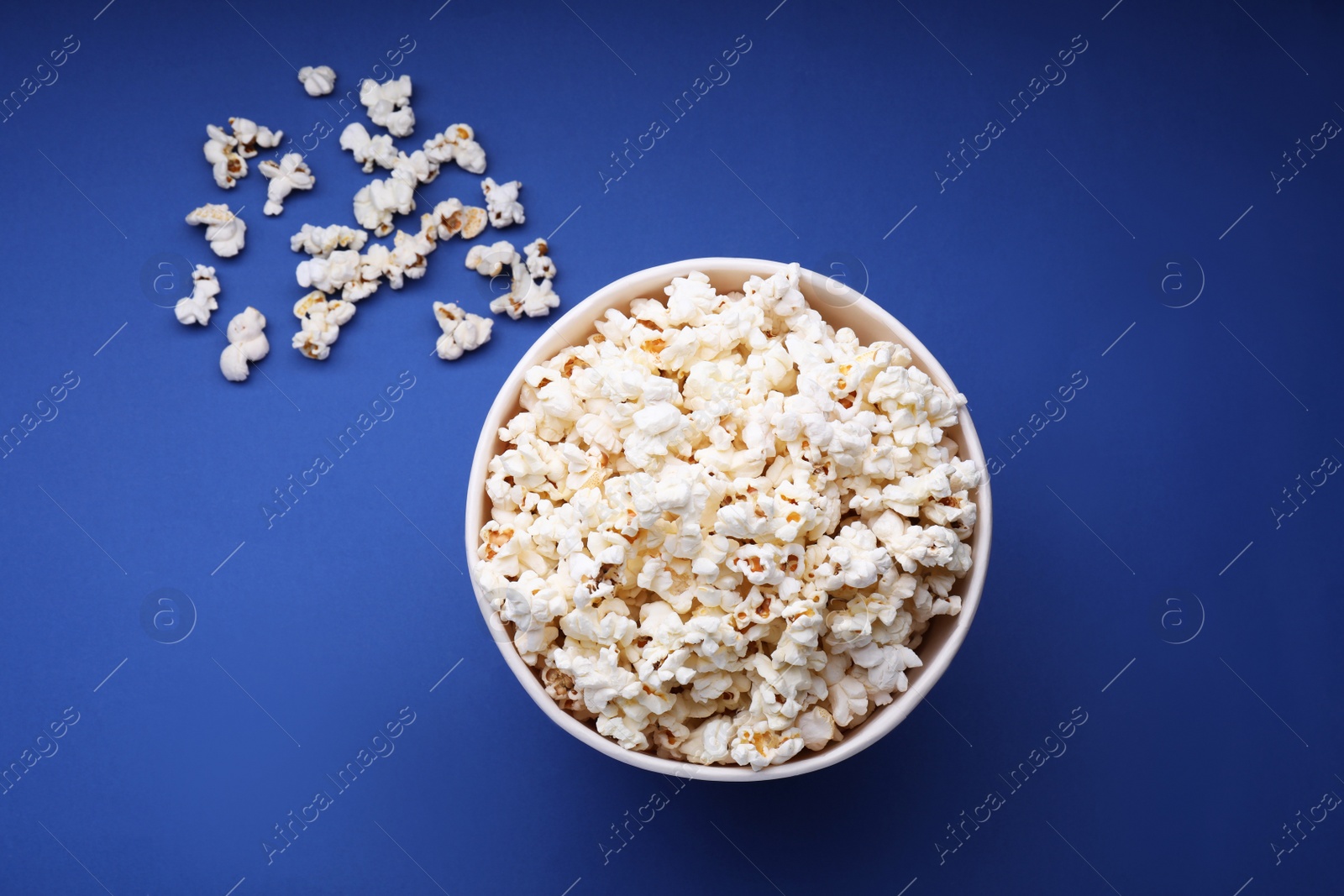 Photo of Bucket of tasty popcorn on blue background, flat lay