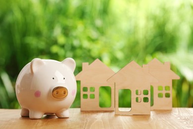 Photo of Piggy bank and house models on wooden table outdoors