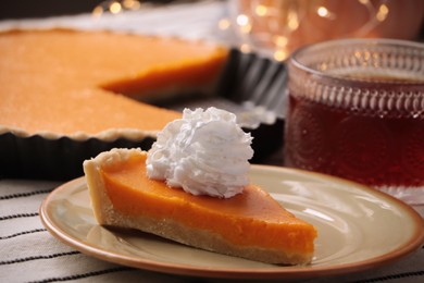 Piece of fresh homemade pumpkin pie served with whipped cream and tea on table