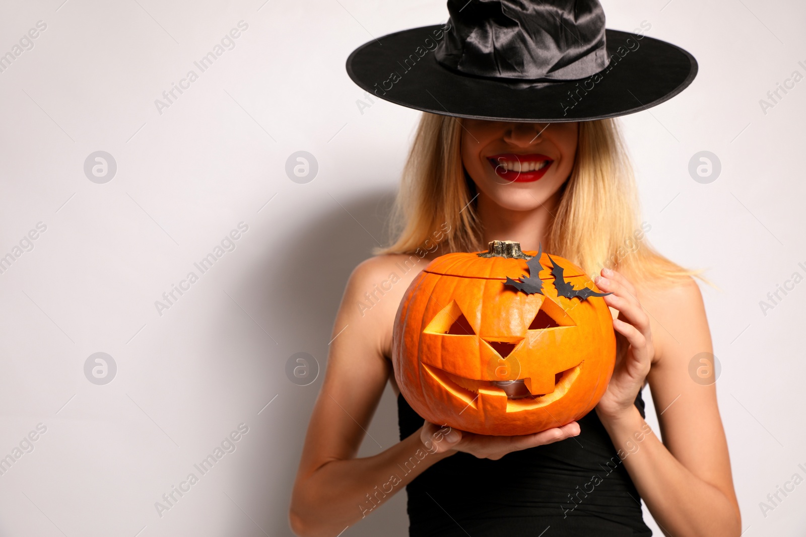 Photo of Beautiful woman in witch costume with jack o'lantern on white background. Halloween party