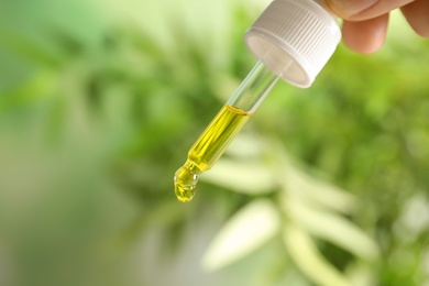 Woman holding pipette with oil on blurred background. Space for text