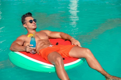 Young man with cocktail and inflatable ring in pool on sunny day