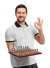 Smiling man holding chessboard with game pieces and showing OK gesture on white background