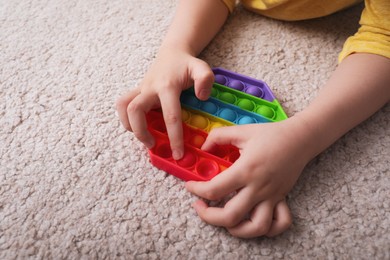 Photo of Little boy playing with pop it fidget toy on floor, closeup