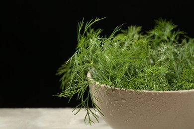 Photo of Bowl of fresh green dill with water drops on light grey table against black background, closeup. Space for text