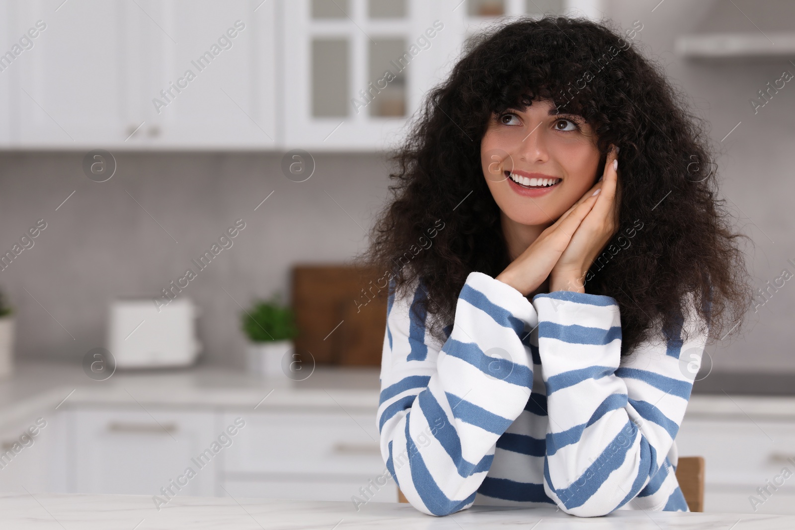 Photo of Portrait of beautiful woman with curly hair in kitchen. Attractive lady smiling and posing for camera. Space for text