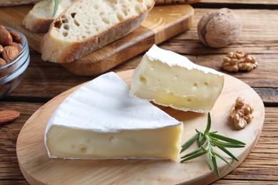 Photo of Tasty cut brie cheese with rosemary, bread and nuts on wooden table