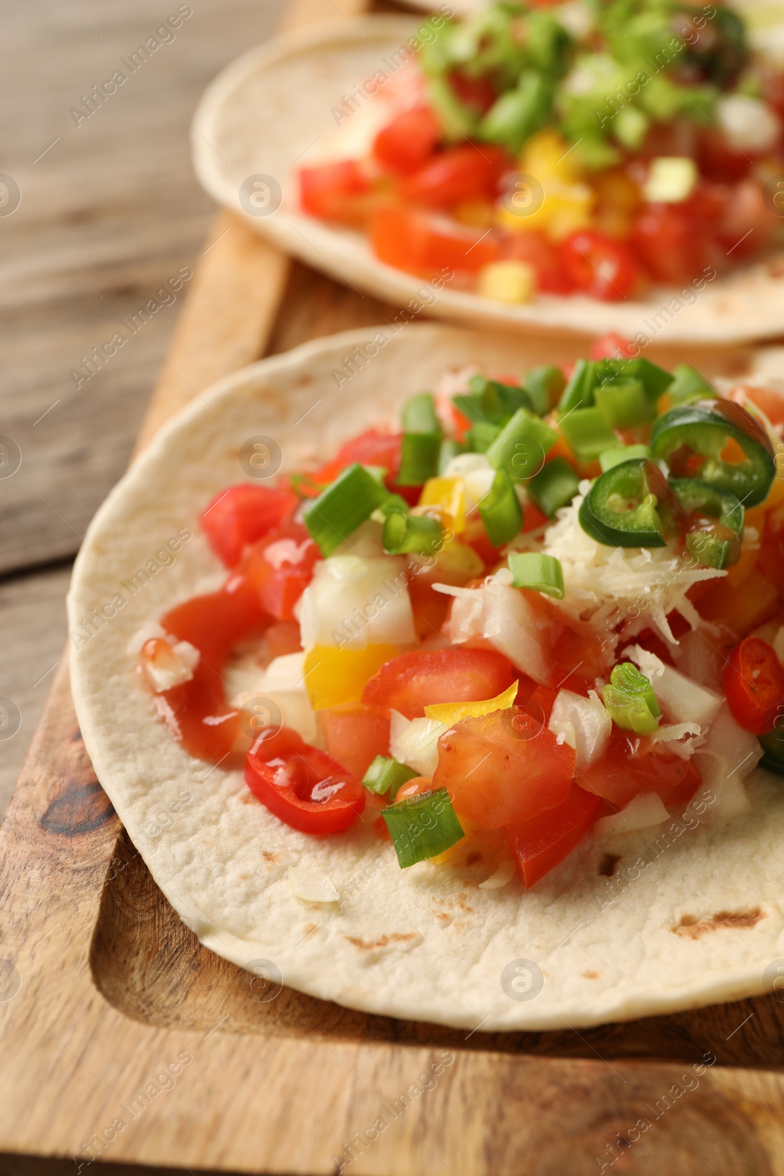 Photo of Delicious tacos with vegetables, green onion, lime and ketchup on wooden table, closeup