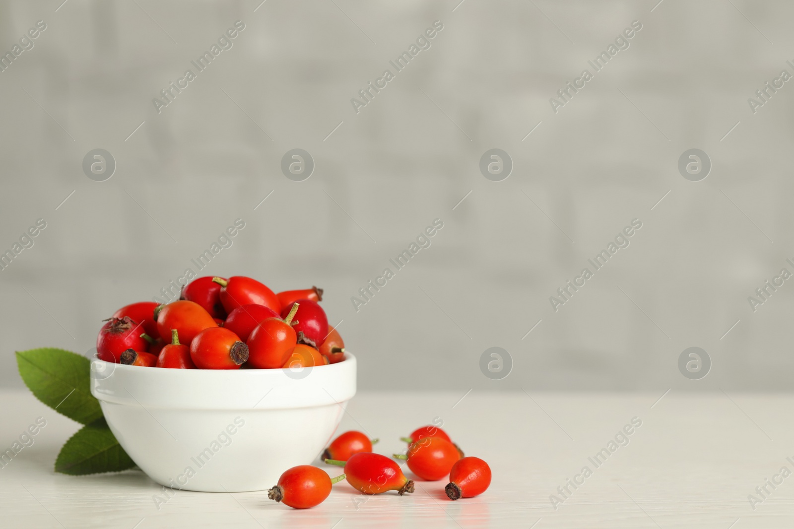 Photo of Ripe rose hip berries with green leaves on white wooden table. Space for text
