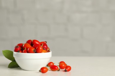 Ripe rose hip berries with green leaves on white wooden table. Space for text