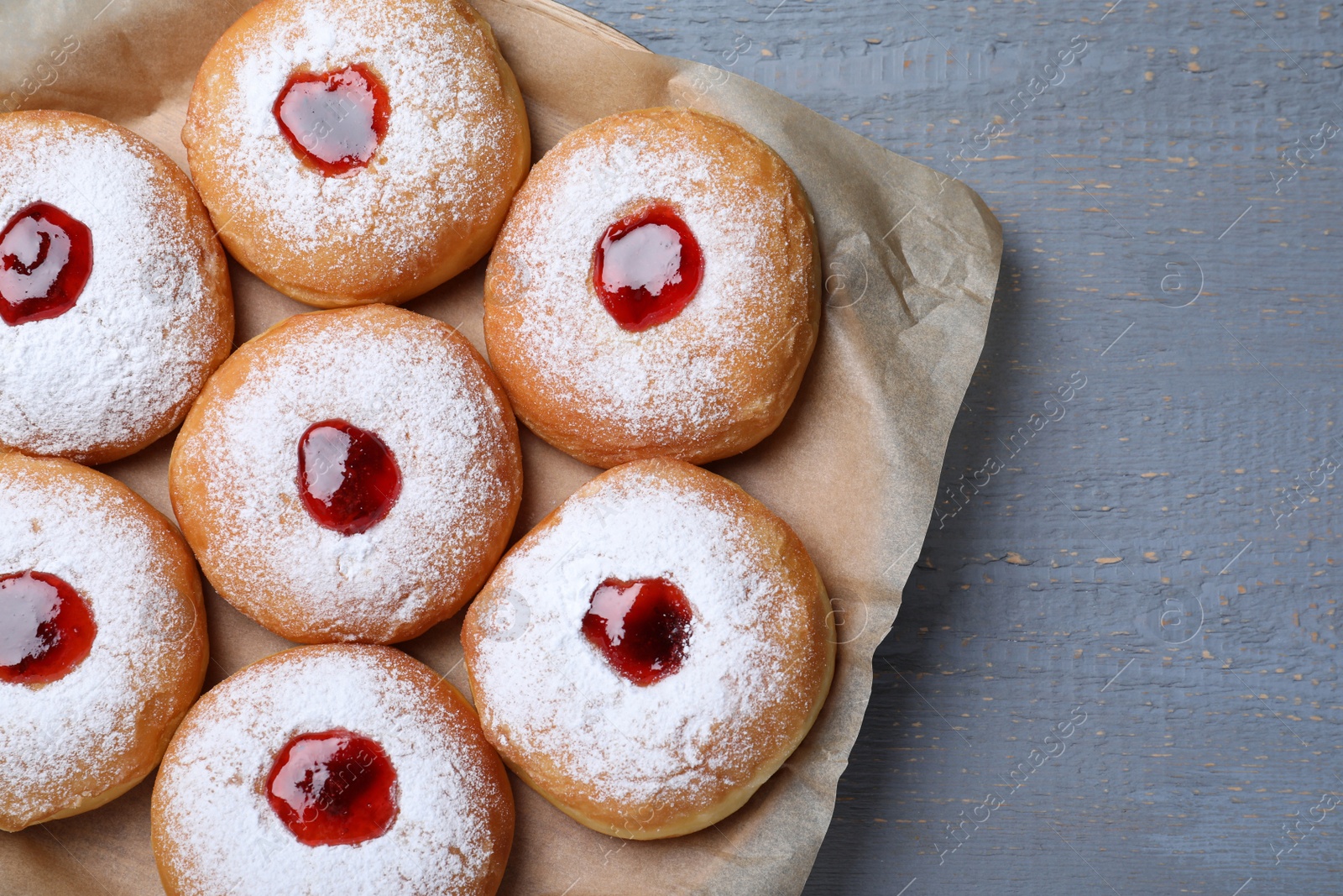 Photo of Hanukkah doughnuts with jelly and sugar powder on grey wooden table, top view