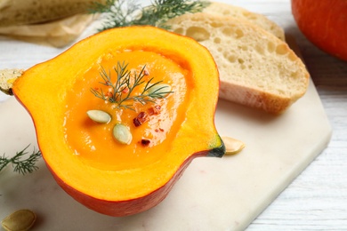 Photo of Tasty cream soup in pumpkin half on white wooden table, closeup