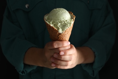 Woman holding green ice cream in wafer cone on black background, closeup