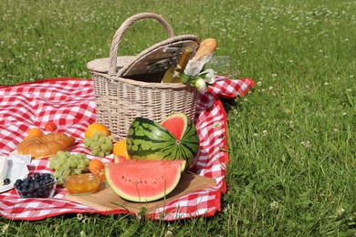 Photo of Picnic blanket with delicious food and wine outdoors on summer day, space for text