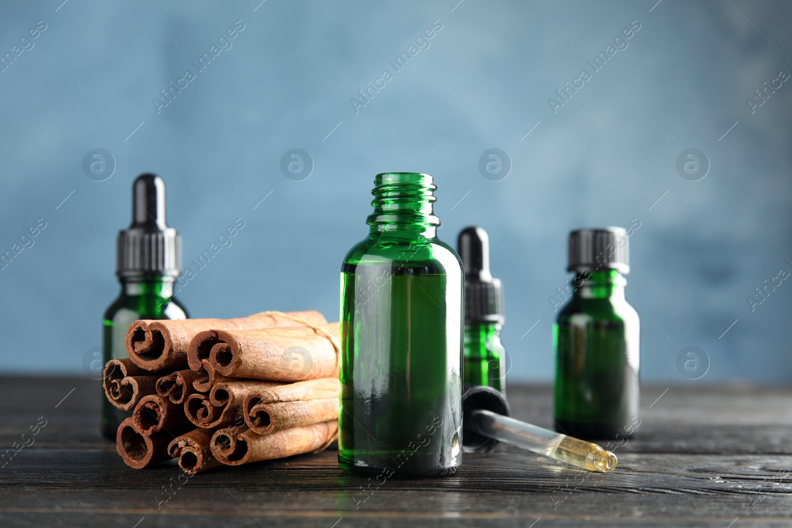 Photo of Bottles with essential oil and cinnamon sticks on wooden table against blue background