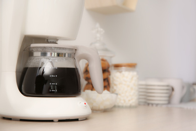 Modern coffeemaker and cups on wooden table indoors