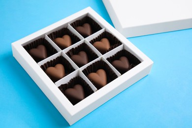 Photo of Tasty heart shaped chocolate candies on light blue background. Happy Valentine's day