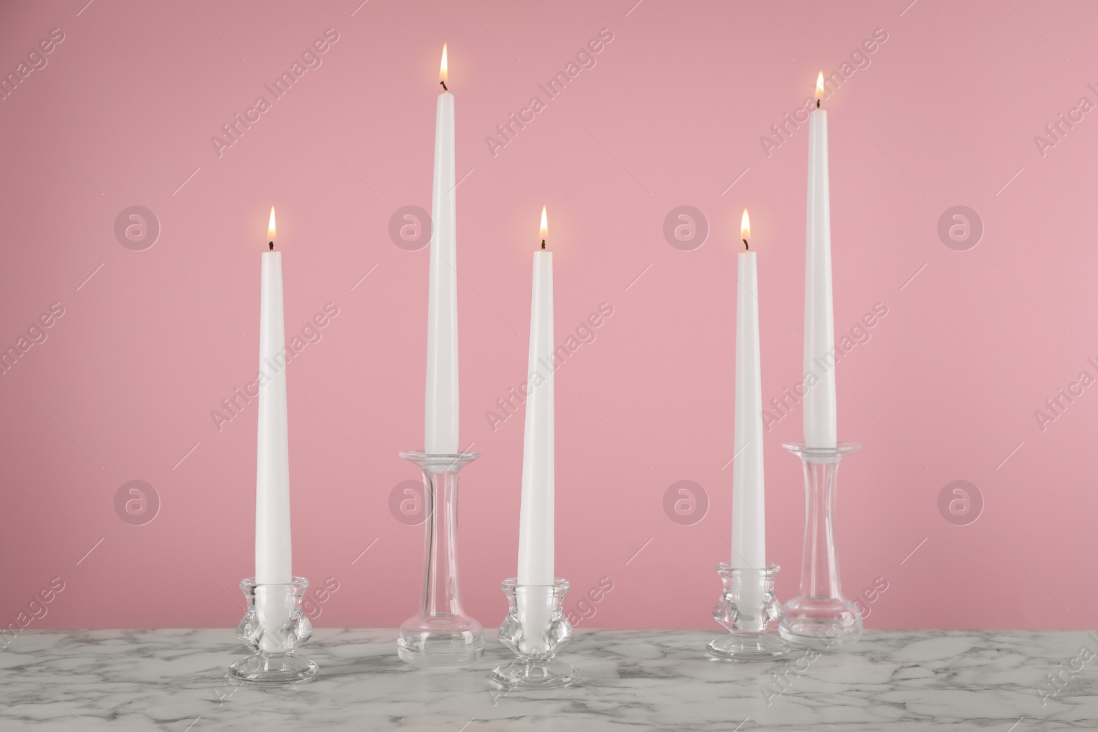 Photo of Elegant candlesticks with burning candles on white marble table