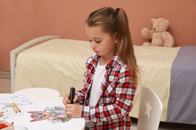 Photo of Little girl coloring antistress page at table indoors