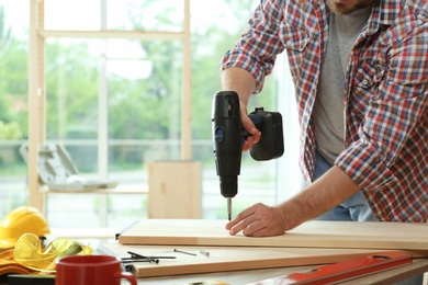 Photo of Man working with electric screwdriver indoors, closeup. Space for text