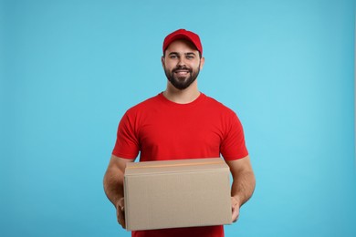 Photo of Happy young courier with parcel on light blue background