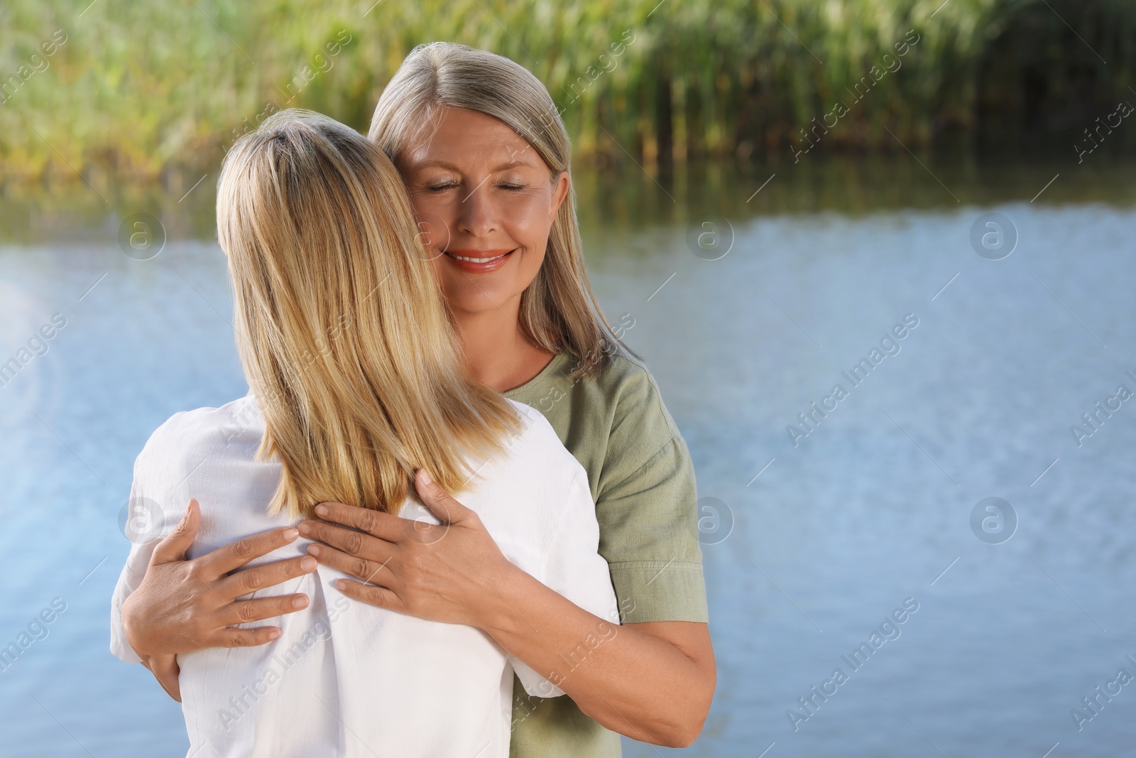 Photo of Family portrait of mother and daughter hugging near pond. Space for text