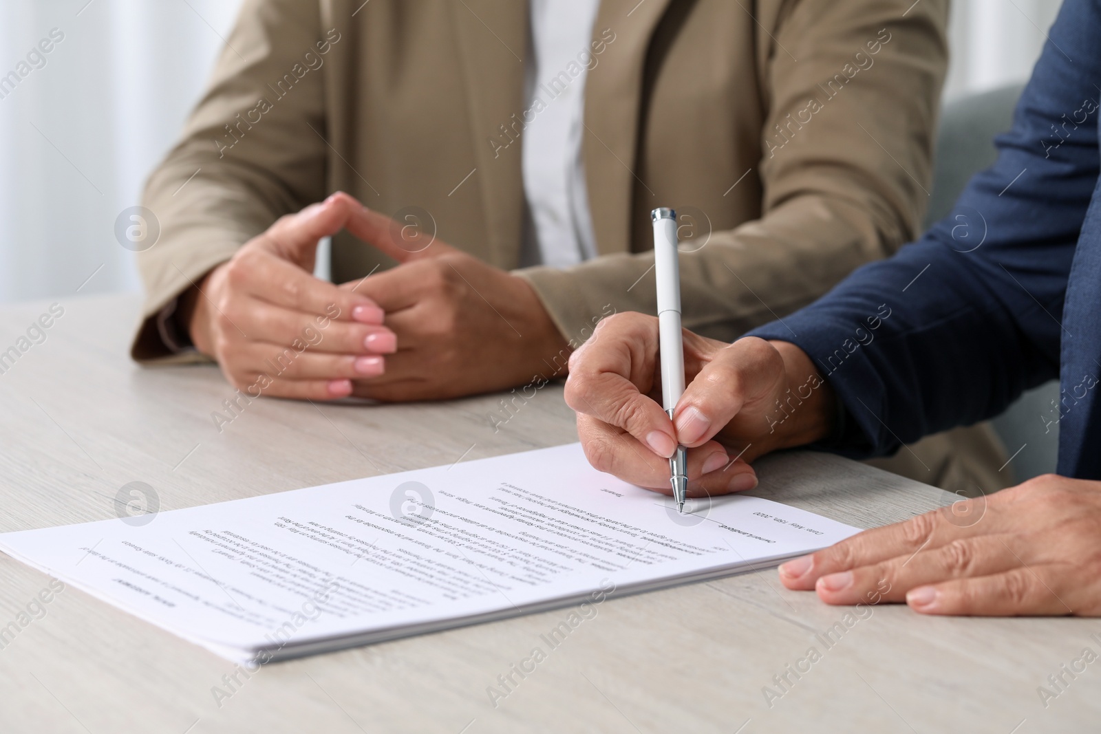 Photo of Signing document. Women at light wooden table indoors, closeup