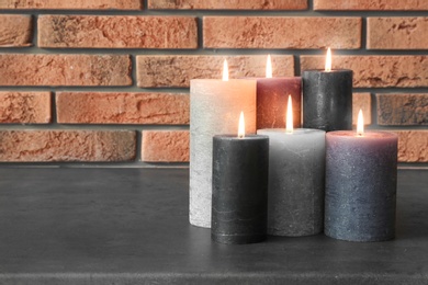 Photo of Burning candles on table against brick wall with space for text