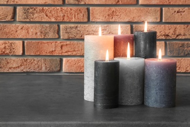 Burning candles on table against brick wall with space for text